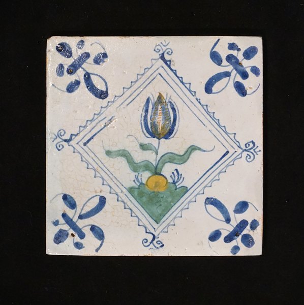 A 17th century polychrome decorated Dutch tile with a flower. Circa 1620-40. 
Size: 13x13cm